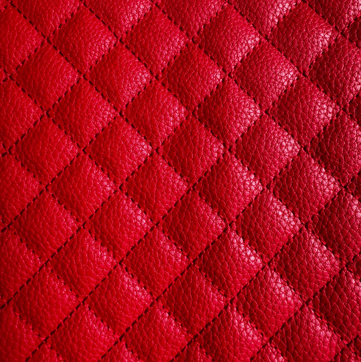 A close-up of bright red quilted leather texture with a repeating diamond pattern and pebbled grain.