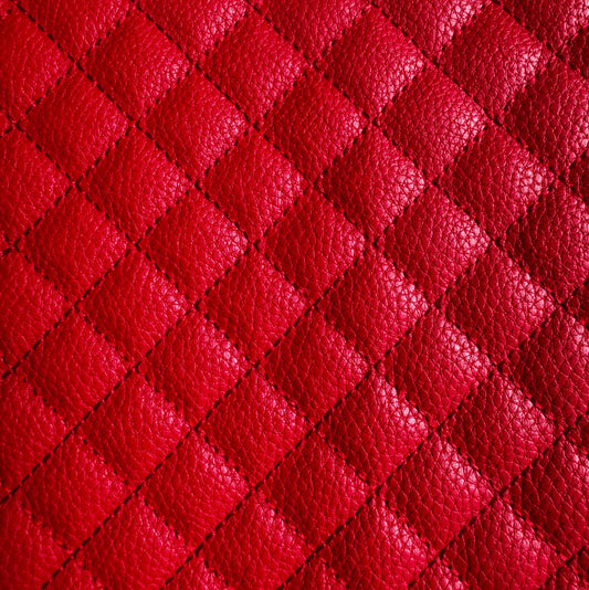 A close-up of bright red quilted leather texture with a repeating diamond pattern and pebbled grain.