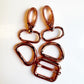 Four rose gold metal hardware components, including two lobster clasps and two D-rings, arranged on a plain white background.