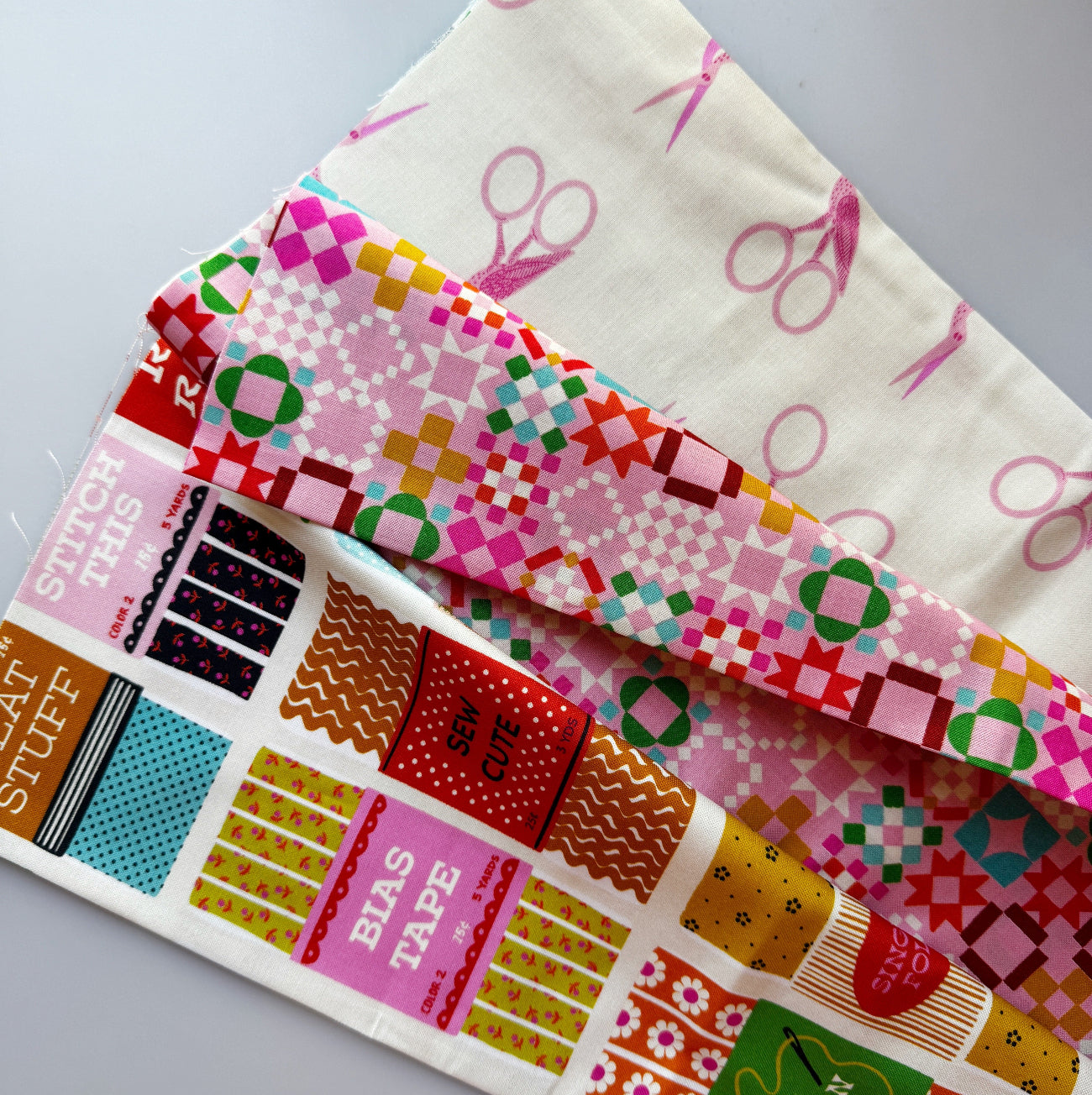 Sewing-themed cotton fabric bundle featuring pink scissors print, colorful geometric quilt-inspired fabric, and sewing notions fabric with bias tape and sewing supplies designs.