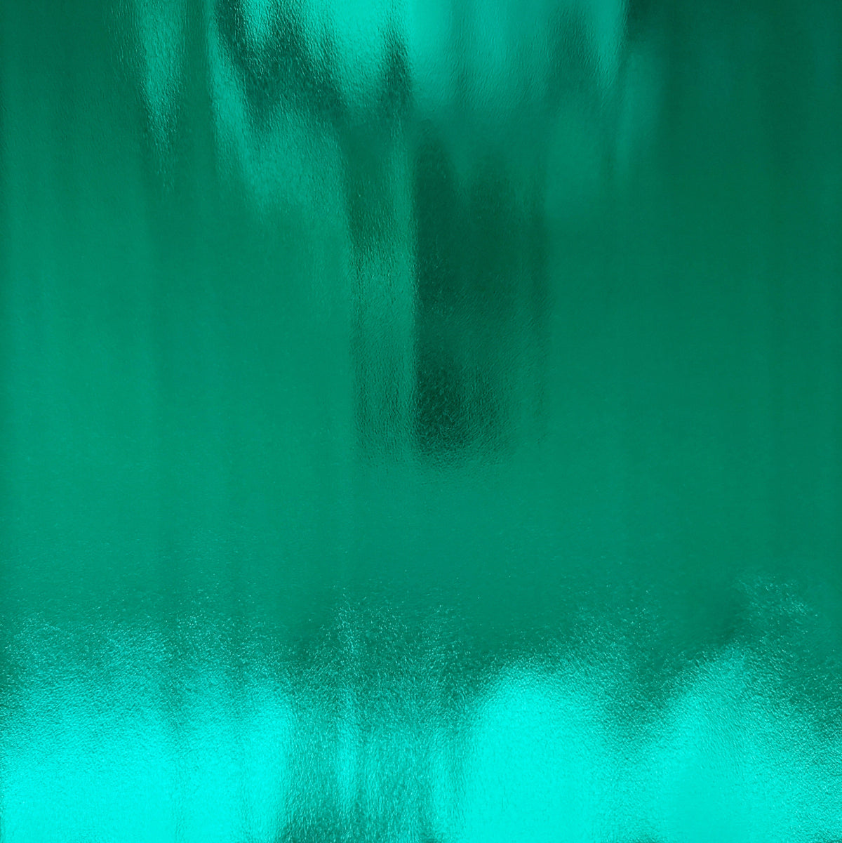 Reflective emerald green metallic vinyl fabric held by hand, showcasing its smooth, high-shine finish against a white background.