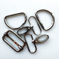 Six polished silver metal hardware components, including rings, loops, and clips, arranged on a plain white background.