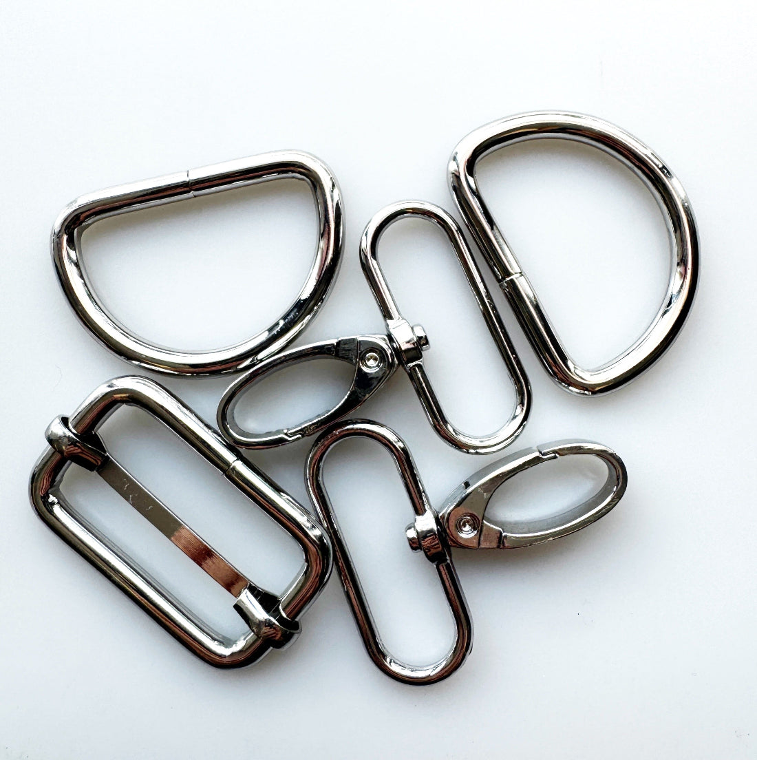 Six polished silver metal hardware components, including rings, loops, and clips, arranged on a plain white background.