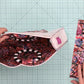 A top-down view of a person's hands holding open a floral zippered pouch to show the patterned lining, with the matching zippered pouch laid flat on a green cutting mat background.
