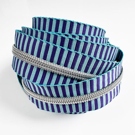 Continuous zipper tape with a purple and light blue vertical stripe pattern, featuring metallic silver coil teeth, coiled against a white background.