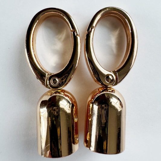 Pair of gold tassel caps with dangling gold pendants on a white background