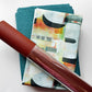 Teal fabric, abstract patterned fabric, and burgundy textured faux leather arranged together for a sewing or bag-making project.