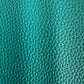 Close-up of a vibrant teal pebbled leather texture, showing a detailed pattern of fine, shimmering creases and raised bumps that capture the light.
