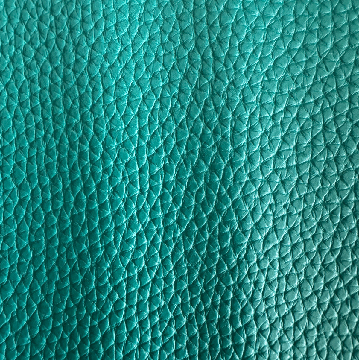 Close-up of a vibrant teal pebbled leather texture, showing a detailed pattern of fine, shimmering creases and raised bumps that capture the light.