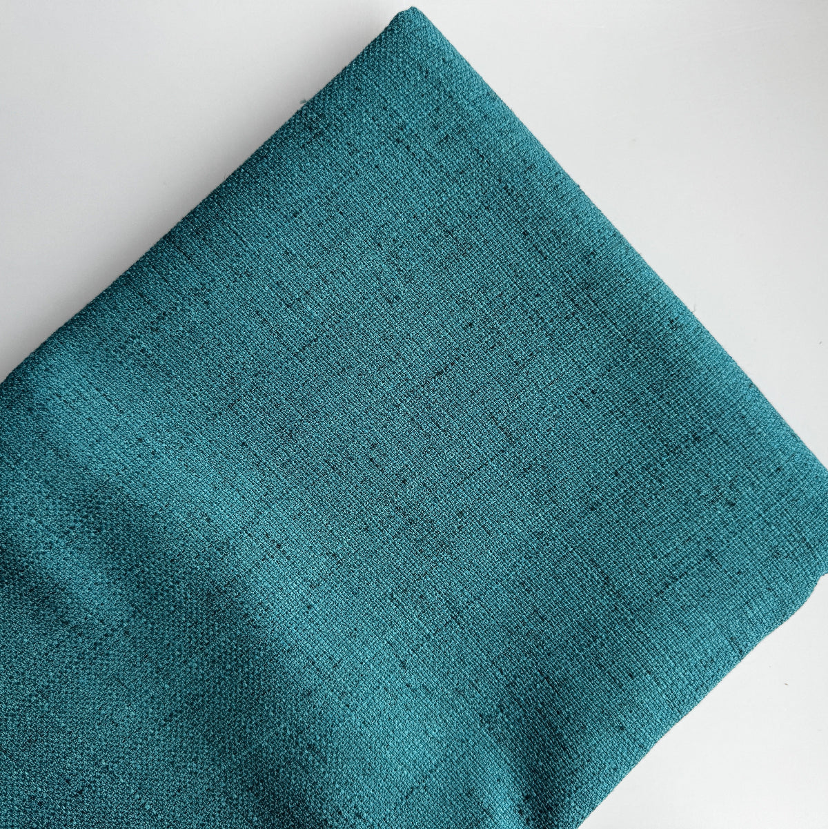 A close-up of folded teal woven fabric with a subtle textured weave, shown on a plain white background.
