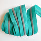 A close-up view of bright teal nylon zipper tape neatly layered and wrapped flatly to showcase several vertical, parallel rows of shiny silver metallic coil teeth against a plain white background.