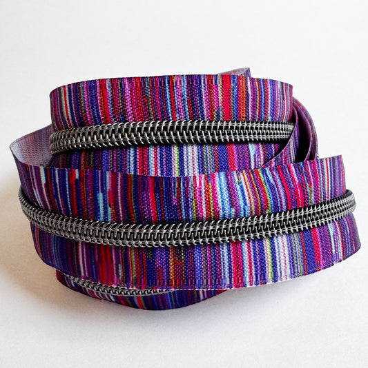 A coiled zipper with a vibrant, multicolored striped fabric tape and a dark metallic zipper track, shown on a plain white background.