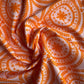 Draped and swirled Treasure Splendour Tang fabric by Bari J for Art Gallery Fabrics, highlighting the texture of the orange medallion pattern on a light pink background.