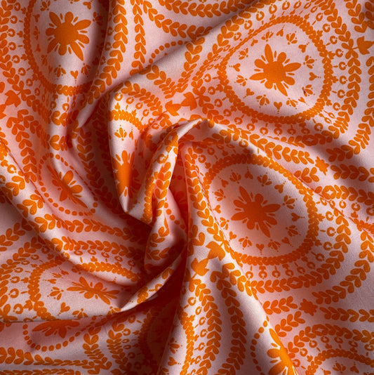 Draped and swirled Treasure Splendour Tang fabric by Bari J for Art Gallery Fabrics, highlighting the texture of the orange medallion pattern on a light pink background.