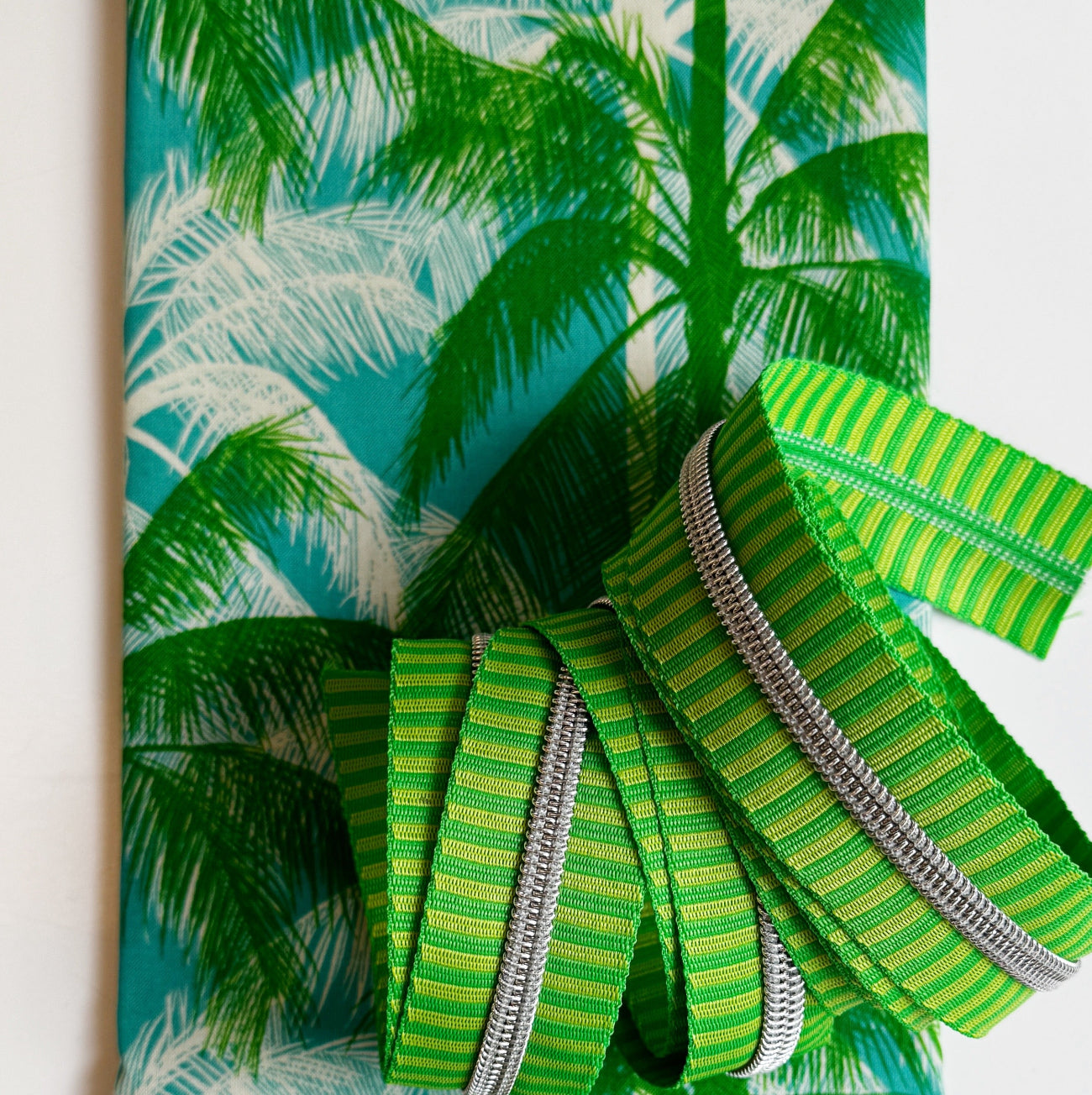 Tropical palm leaf cotton fabric paired with green striped webbing and silver zipper tape for sewing handbags, totes, crossbody bags, and handmade accessories.