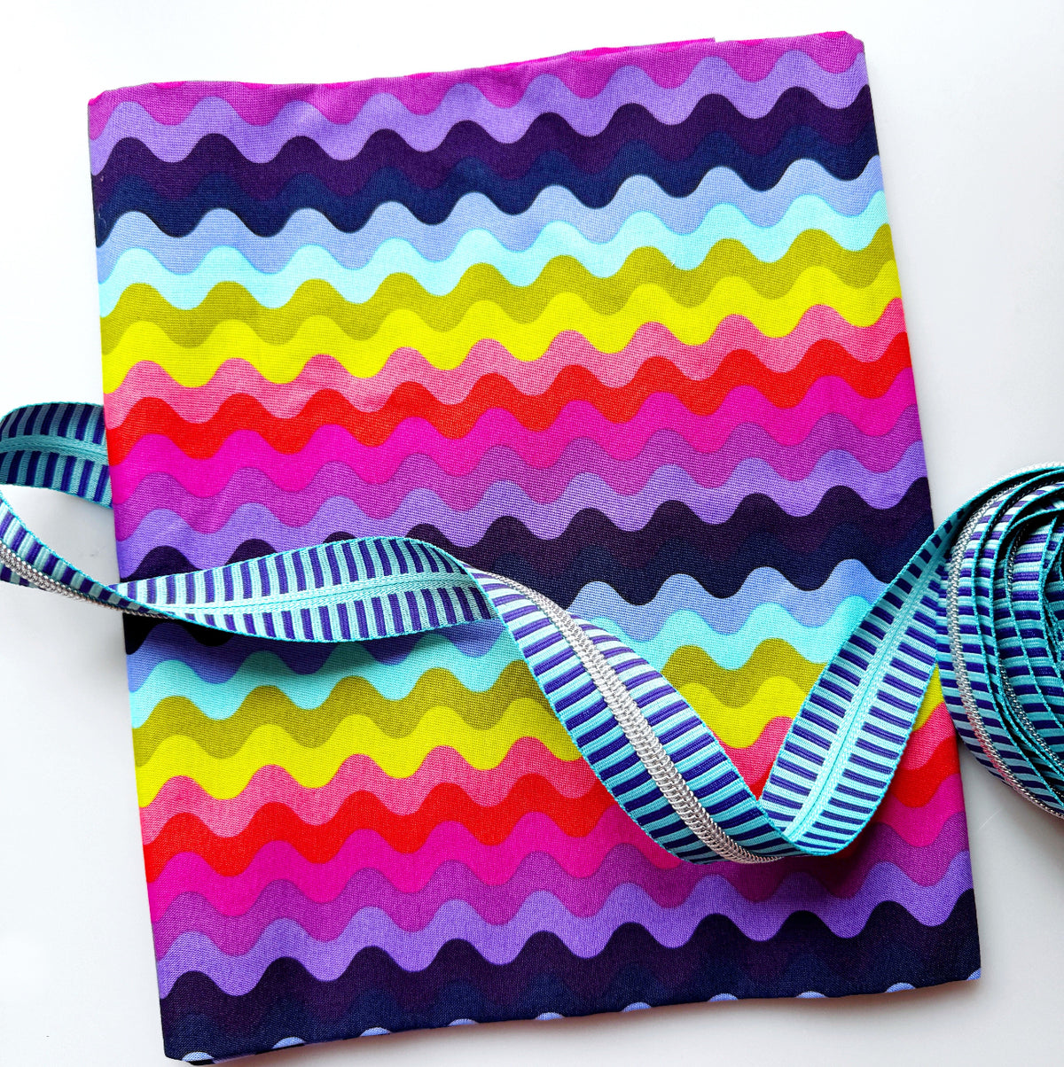 Colorful Tula wavy stripe fabric with pink, purple, blue, yellow, and red stripes paired with striped zipper tape for sewing.