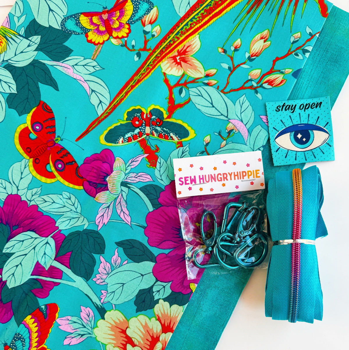 Turquoise floral and butterfly fabric with matching teal zipper, silver bag hardware, and sewing accessories for DIY bag making