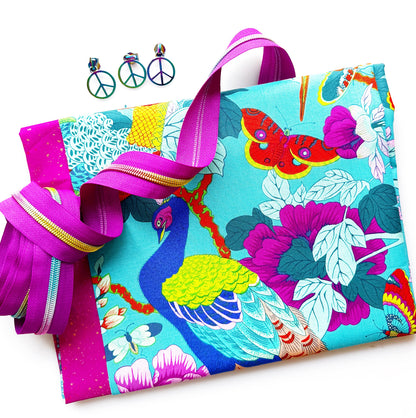 Turquoise cotton fabric featuring colorful peacocks and tropical flowers paired with fuchsia zipper tape, coordinating fabric, and iridescent peace sign hardware for bag making and sewing projects.