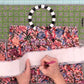 A person's hands are shown folding a white paper template over a colorful floral patterned fabric, with a black and white striped circular ring and a green gridded cutting mat in the background.