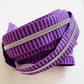 Number 5 continuous nylon coil zipper tape featuring a monochromatic dark and medium purple striped jacquard woven pattern with metallic silver teeth, loosely coiled against a white background.