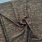A close-up of draped fabric with a dark brown base and an all-over textured gold abstract pattern, gathered in the center to show its drape and sheen.