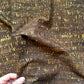 A close-up of dark brown fabric with a textured, distressed pattern of yellow and gold vertical streaks, held by a hand in the bottom-left corner.