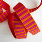 Closed up shot of 1.5-inch wide jacquard woven webbing strap showcasing a vibrant hot pink and orange horizontal stripe pattern, loosely coiled against a white background.