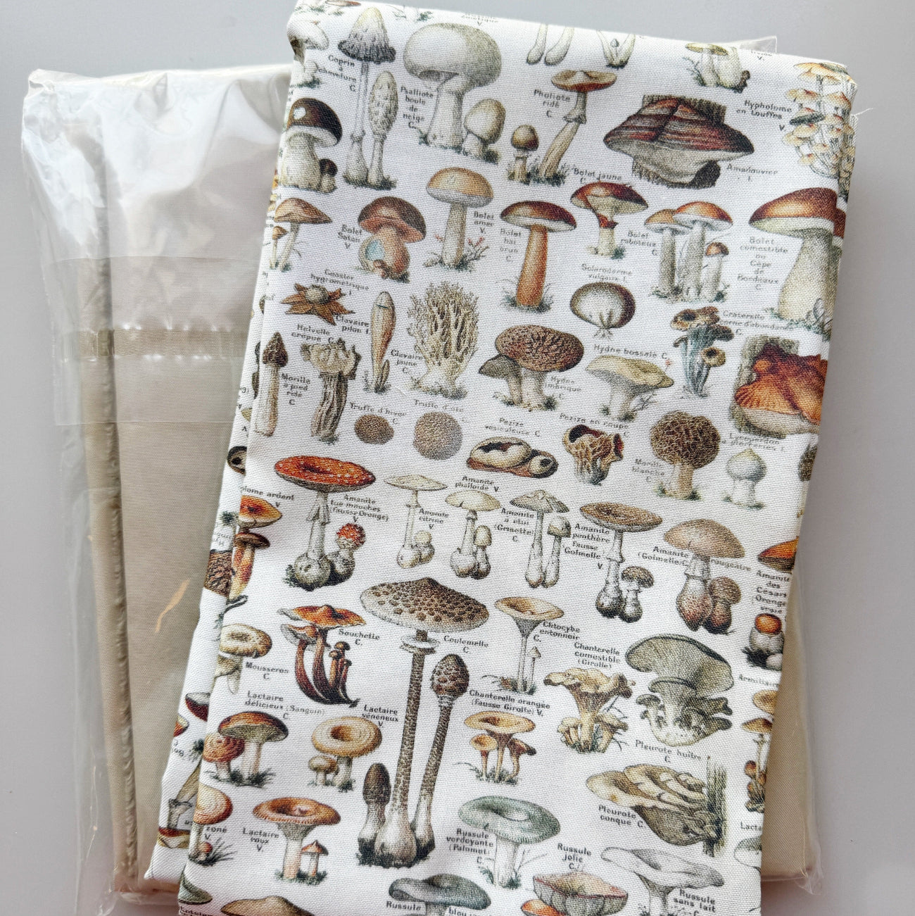 White fabric featuring a detailed vintage-style mushroom and fungi illustration print, layered over white fabric.