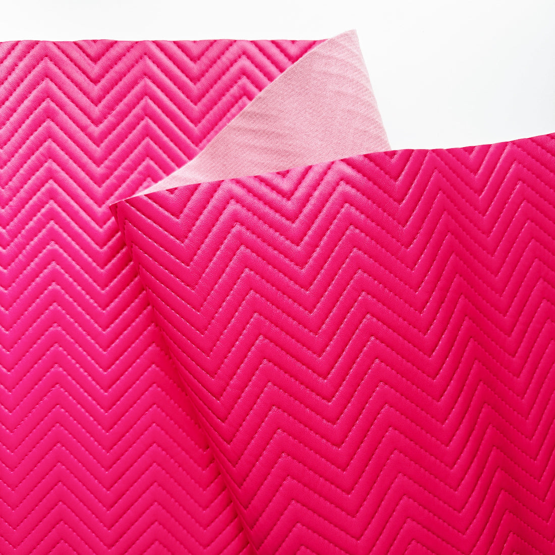 Bright pink fabric with a raised chevron pattern, folded over to show the lighter underside, on a plain white background.