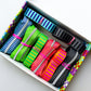 A box of colorful striped elastic bands or straps, arranged diagonally. The bands come in multiple vibrant colors including blue, green, pink, orange, and black, each tied with a small pink elastic band, set against a clean white background.