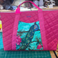 Pink quilted bag with peacock design on a cutting mat