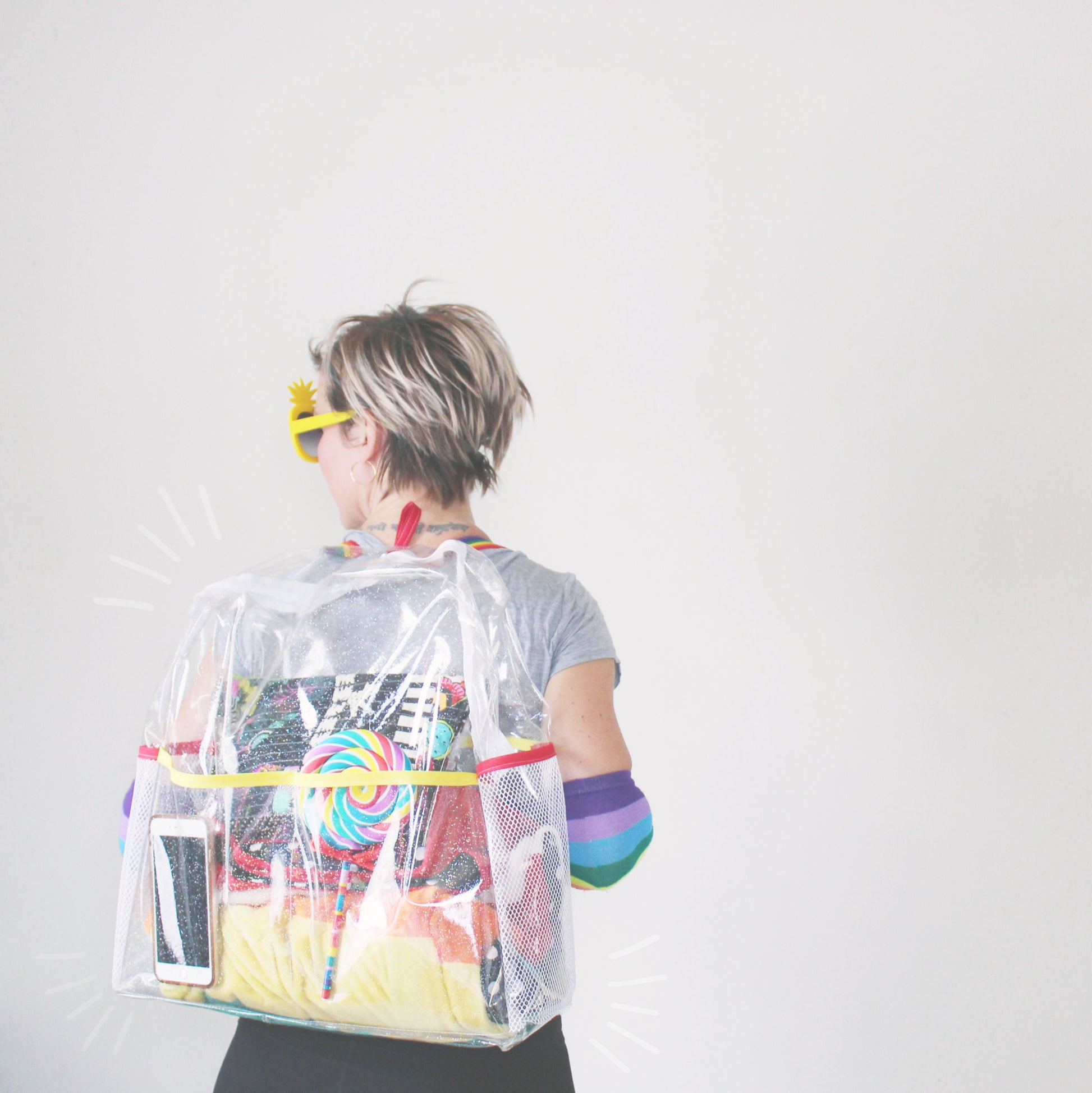 Person wearing a clear backpack with colorful contents on a plain background