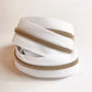 A coiled roll of white zipper tape with metallic gold-toned teeth, photographed on a plain light background.