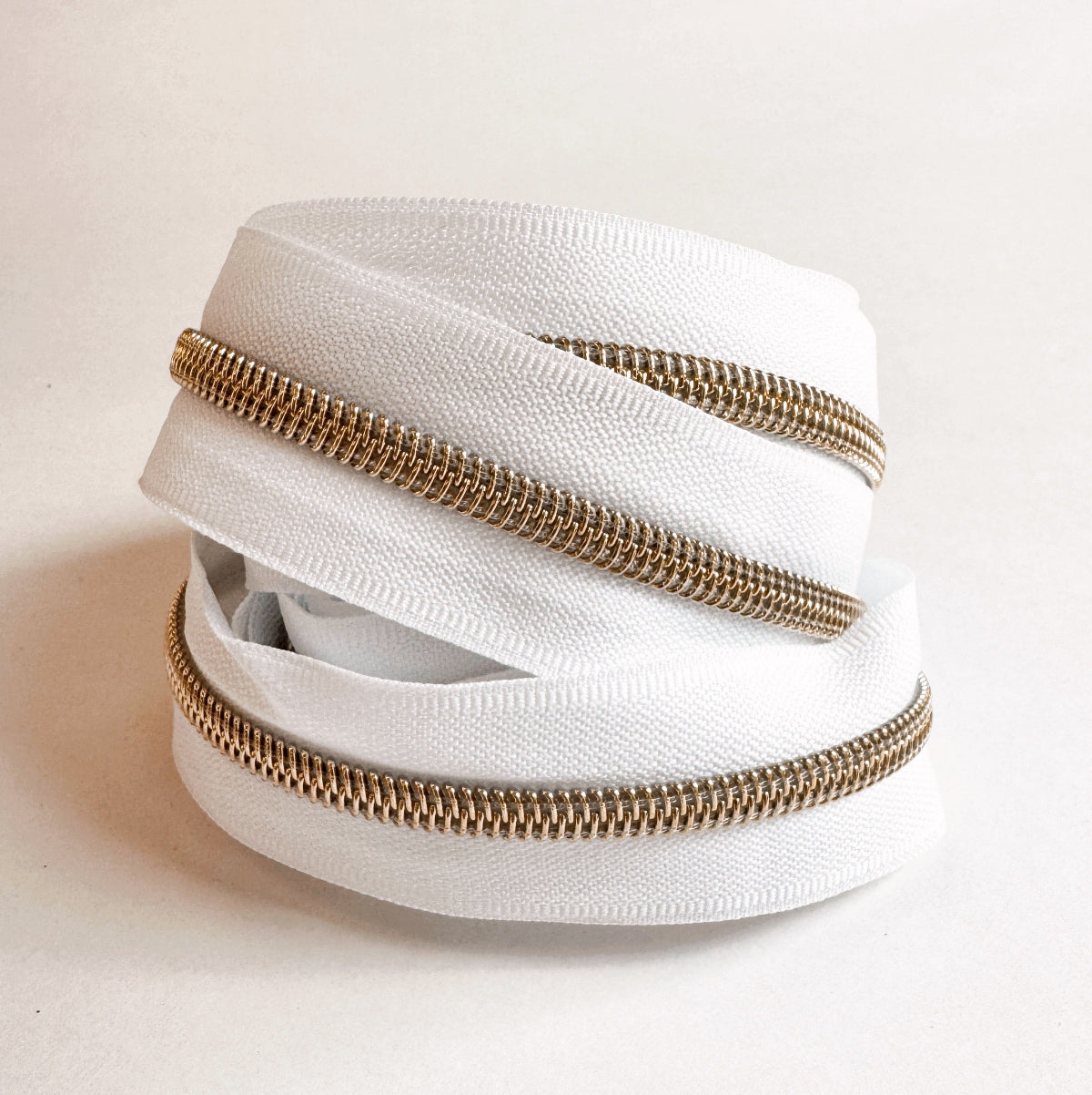 A coiled roll of white zipper tape with metallic gold-toned teeth, photographed on a plain light background.
