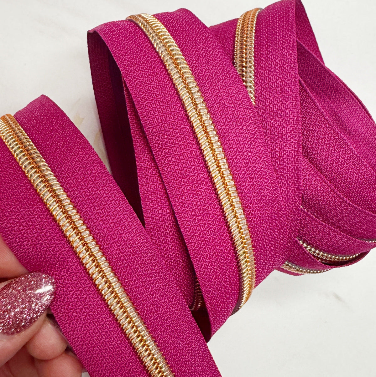 Close-up of pink zippers with gold trims held by a hand on a white background