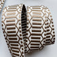 A close-up of a woven ribbon or trim with a geometric pattern in brown and off-white, rolled into loops on a light gray background.