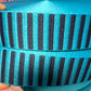 A close-up of a woven ribbon or trim with alternating vertical stripes in bright turquoise blue and dark navy blue.