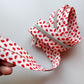 A close-up of a silver metal zipper with a white fabric tape printed with a red strawberry pattern, held by a hand against a plain light gray background.