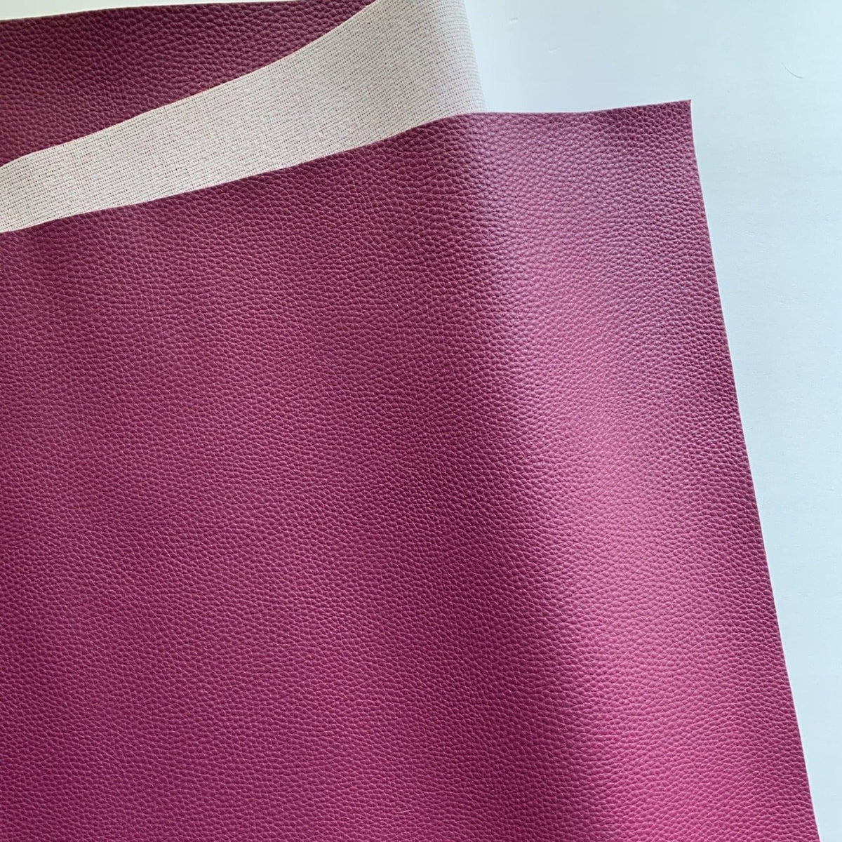Berry magenta-purple pebbled faux leather vinyl fabric with lychee grain and cream woven backing
