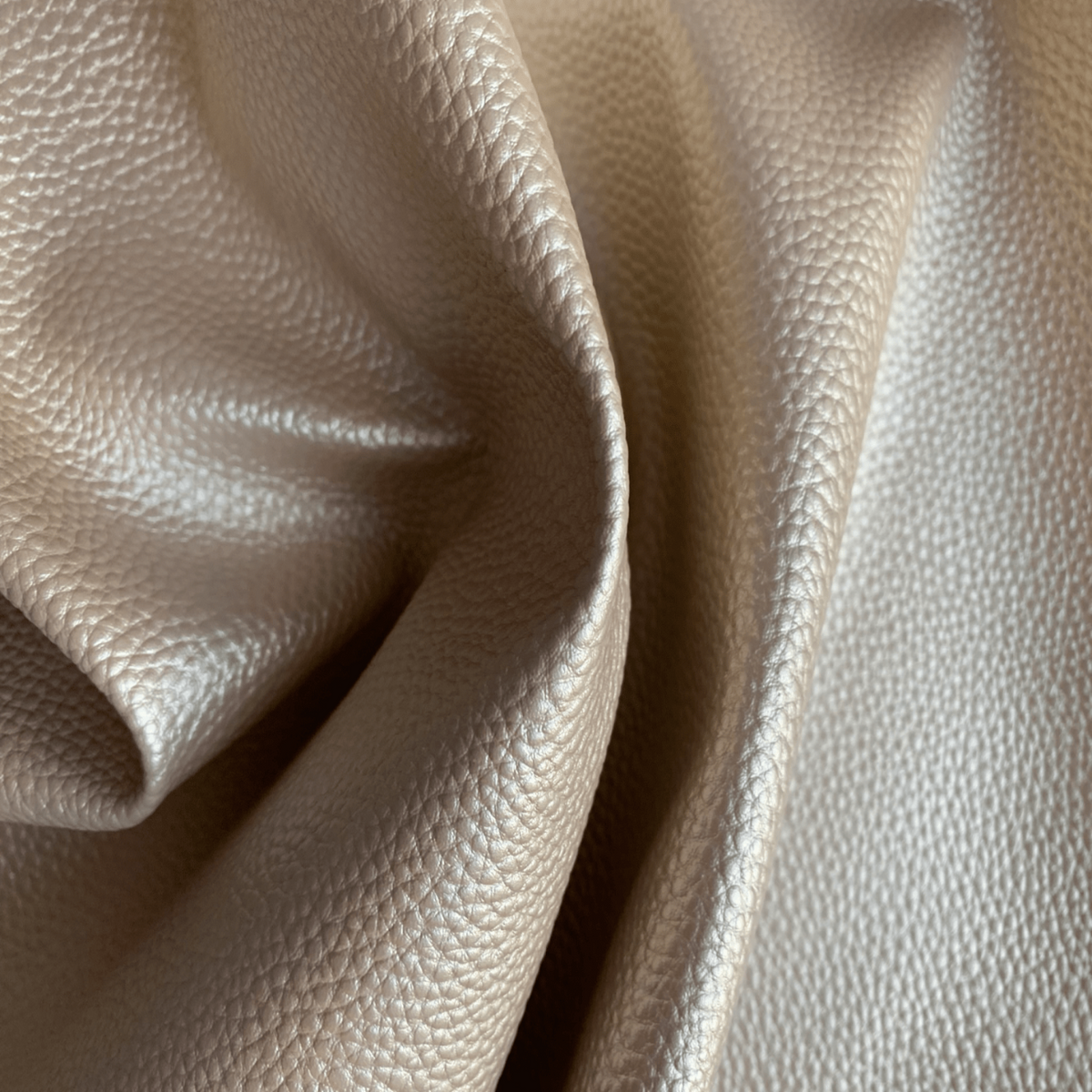 Close-up of draped faux leather fabric with a pebbled texture in a metallic champagne beige color.
