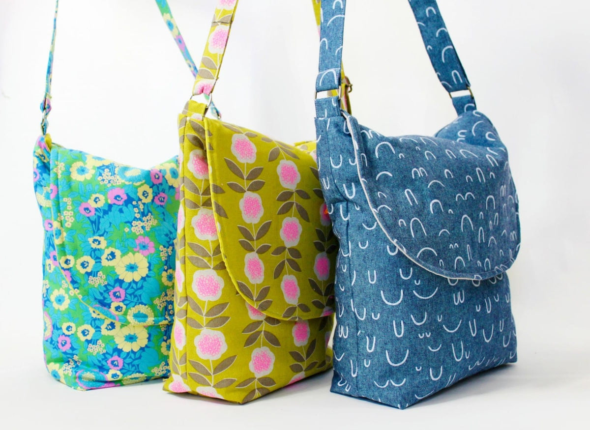 Three handmade fabric messenger bags with long shoulder straps are lined up against a plain white background