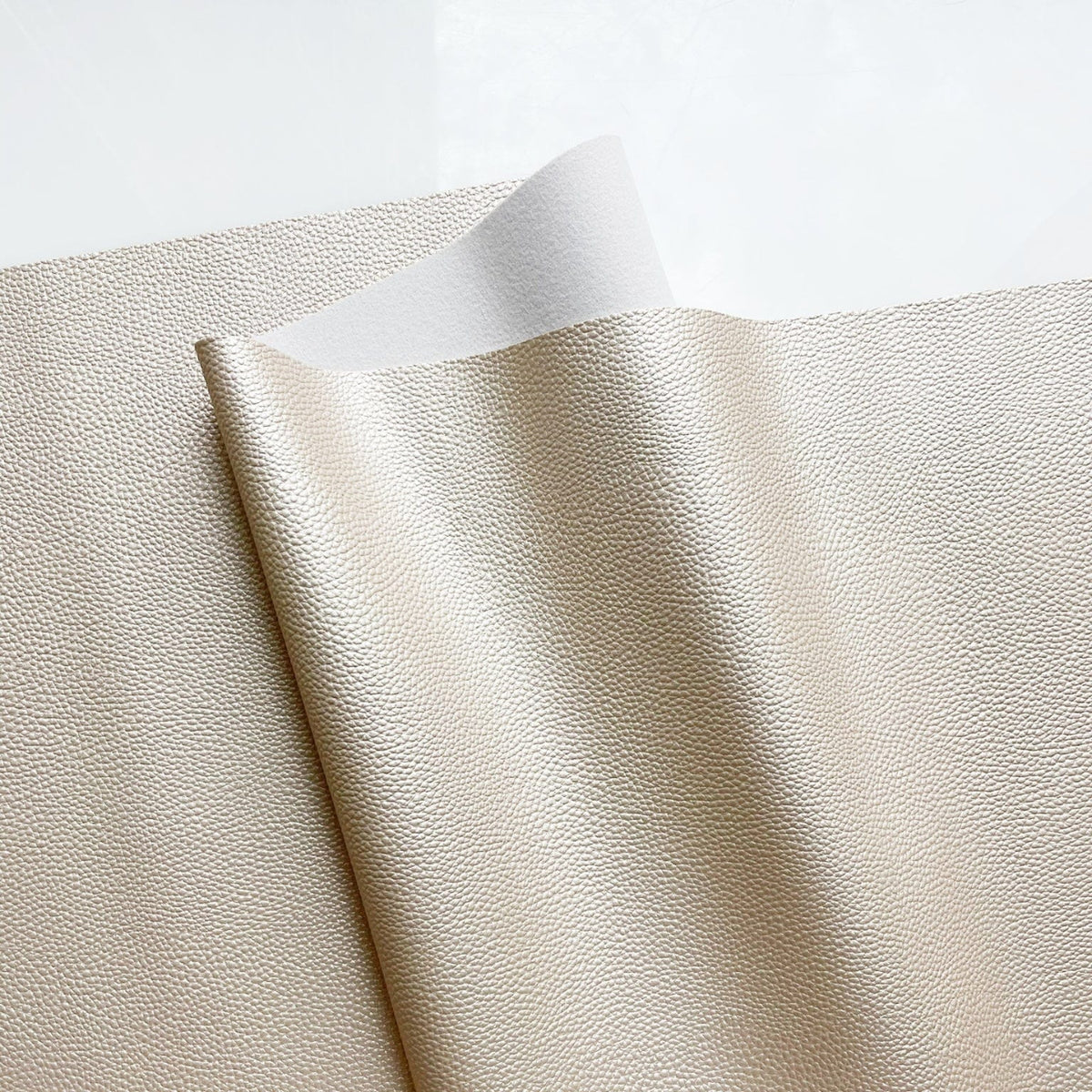 Cose-up of Champagne Moonglow vinyl faux leather fabric, showing its finely pebbled grain texture and subtle metallic sheen.