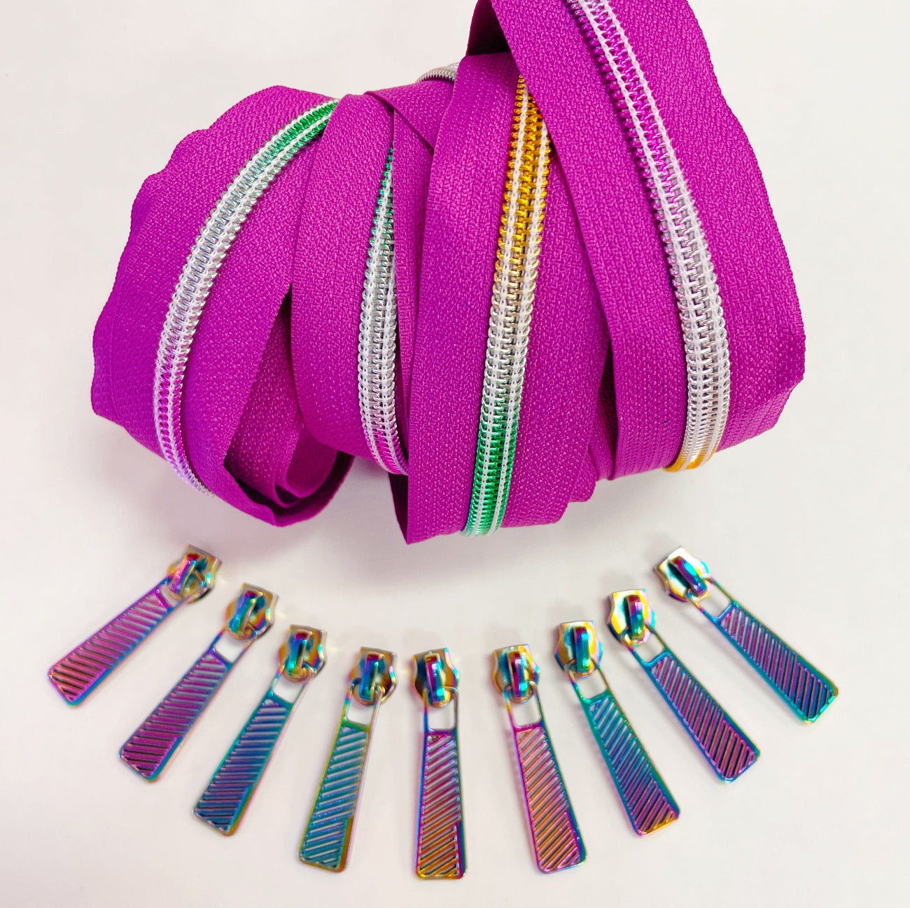 Fuchsia continuous zipper tape with coordinating iridescent rainbow zipper pulls displayed for bag making, purse sewing, and DIY sewing projects.