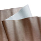 Close-up of a textured faux leather fabric sheet showing a metallic bronze or taupe color on one side with a fine pebbled grain, and a smooth, light gray fabric backing on the underside.