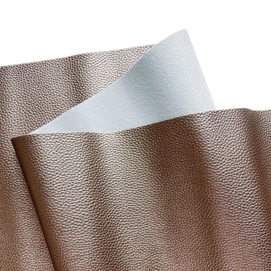 Close-up of a textured faux leather fabric sheet showing a metallic bronze or taupe color on one side with a fine pebbled grain, and a smooth, light gray fabric backing on the underside.